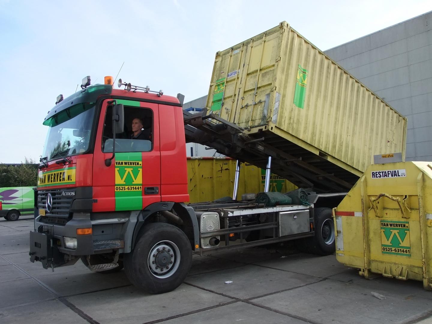 Dezelfde containerauto laadt de gele zeecontainer, met daarachter de containers voor karton en restafval