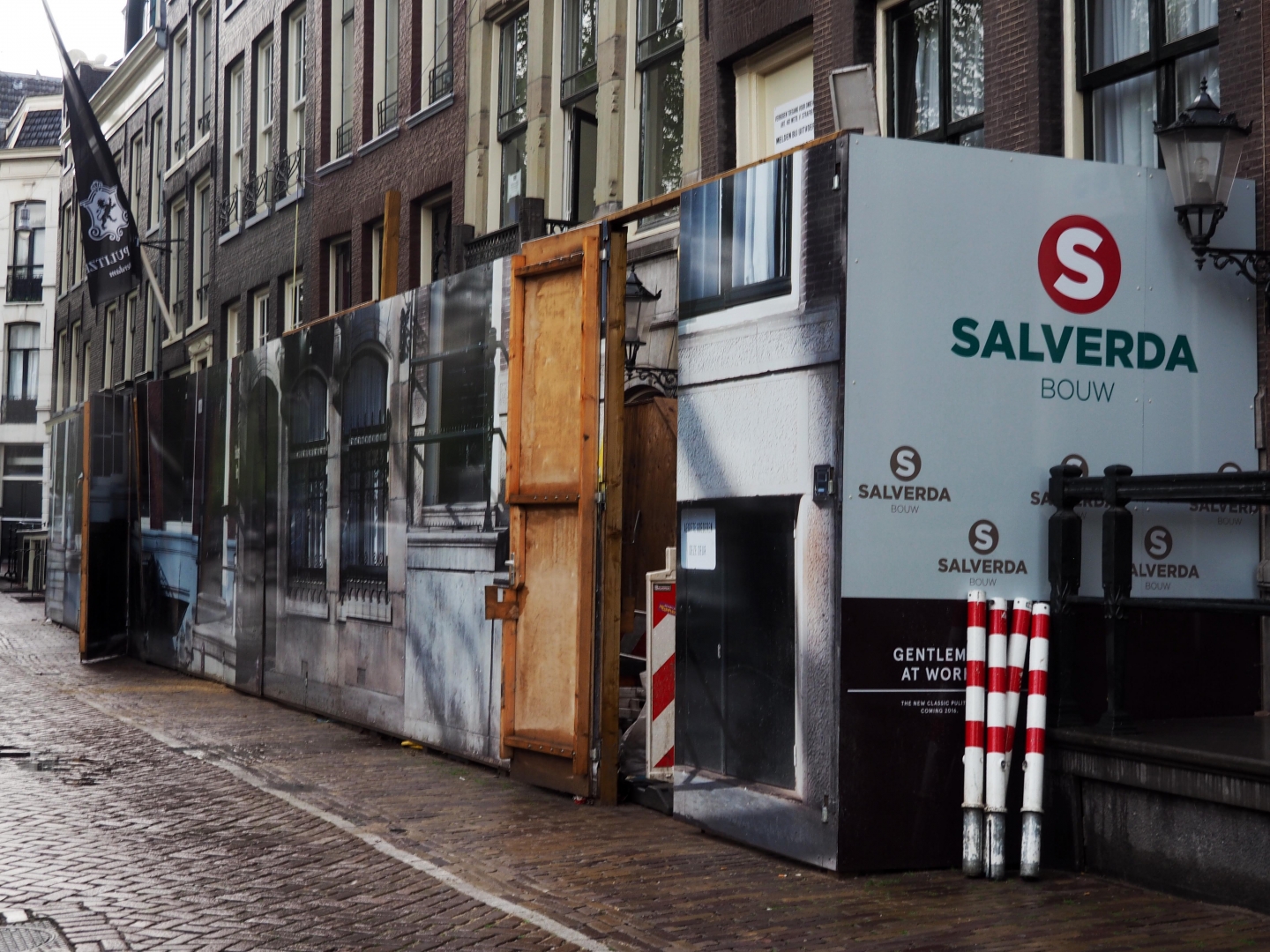Een bouwschutting van Salverda Bouw langs de gevel van het Pulitzer Hotel, beplakt met foto's van de panden erachter